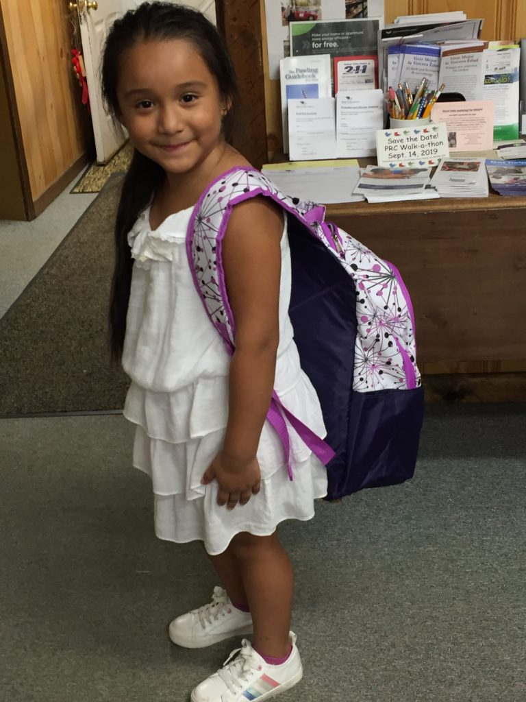 chid in white dress with backpack filled with school supplies