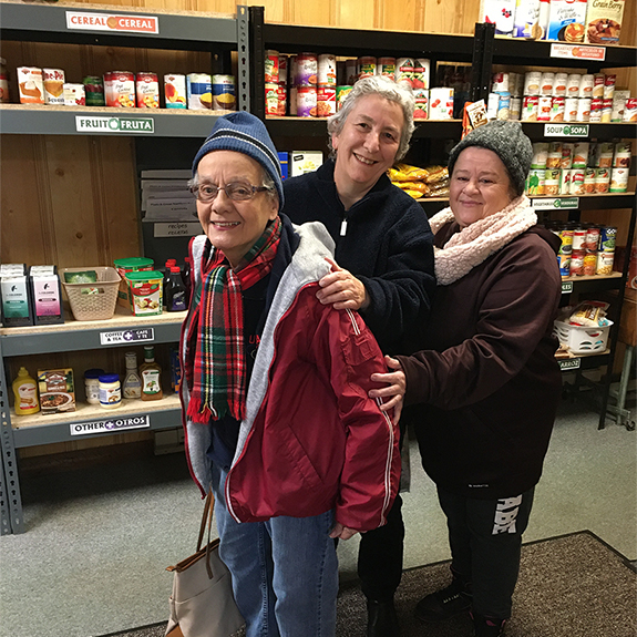 two woman in winter coats with third woman helping them with groceries