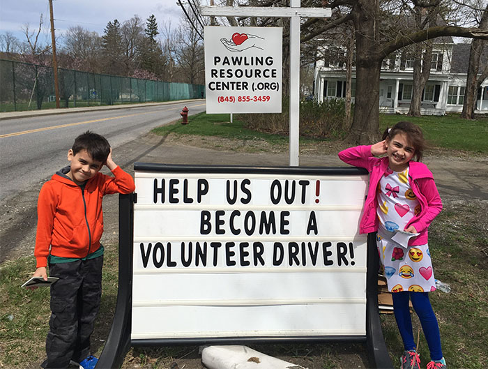 boy and girl leaning on sign help us out volunteer